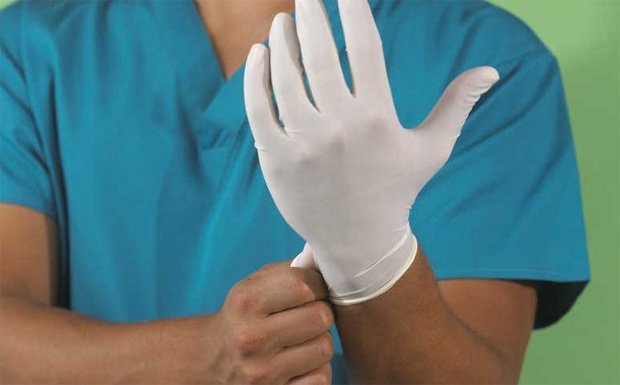 Врач надевает на левую руку медицинскую перчатку