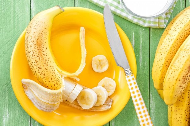 На желтой тарелке лежит очищенный и нарезанный банан и нож с желтой ручкой
