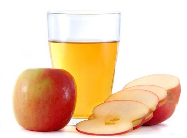 На столе стакан с яблочным уксусом, целое и нарезанное яблоко