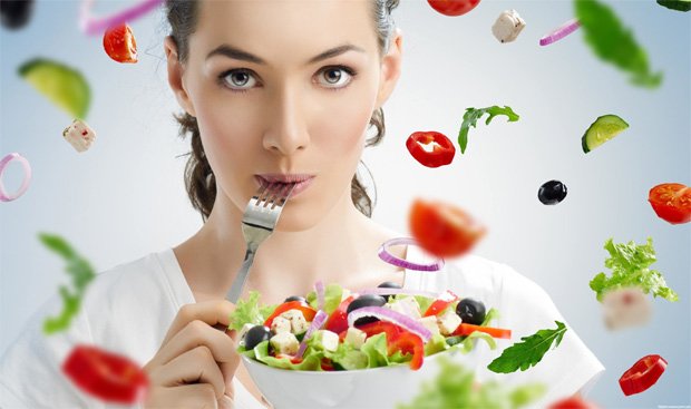 Девушка ест из миски полезный салат на фоне других овощей