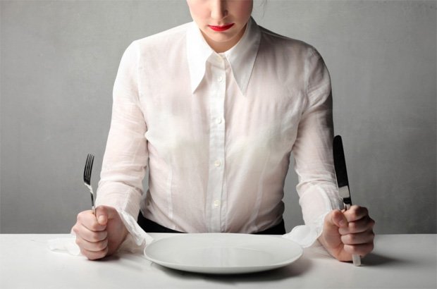 Девушка с вилкой и ножом в руках сидит напротив пустой тарелки