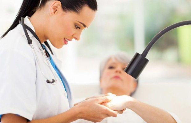 Женщина врач под лампой рассматривает руку пациентки