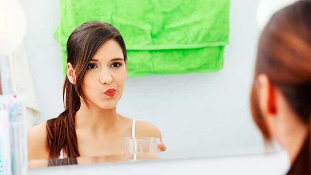 Девушка перед зеркалом в ванной полощет рот раствором