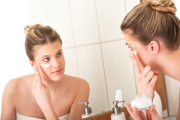 Девушка перед зеркалом в ванной наносит на лицо крем