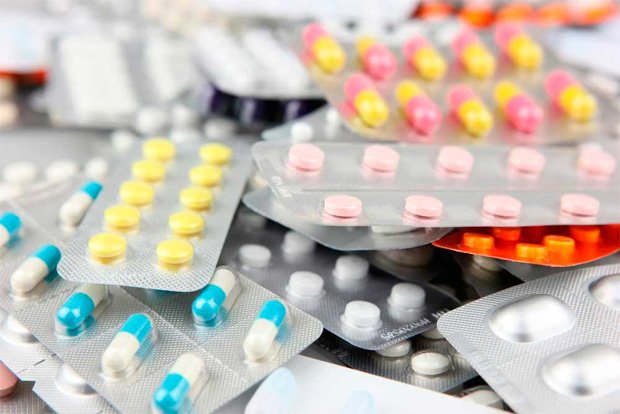 На столе в упаковках лежит большое разнообразие лекарств в таблетках