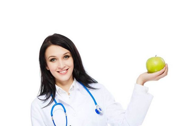 Девушка с медицинском халате держит в руке зеленое яблоко