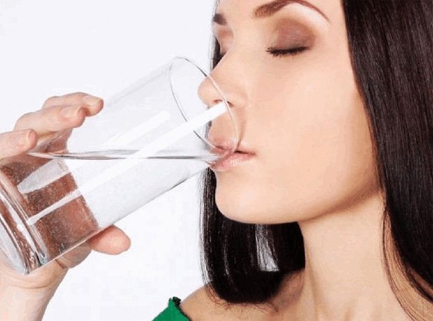 Девушка пьет воду из высокого прозрачного стакана