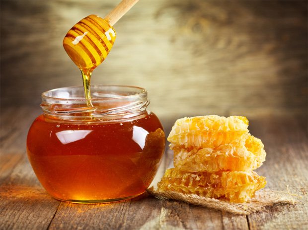 На столе в баночке свежий мед, палочка и медовые соты