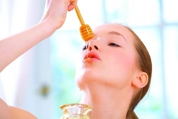 Девушка капает на свои губы мед с медовой ложечки