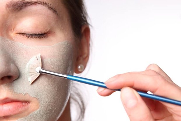 Девушке наносят на лицо кисточкой лечебную маску для кожи