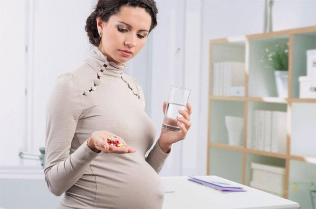 Беременная женщина держит в руке стакан воды и горсть лекарств