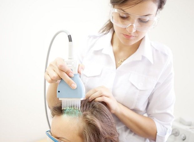 Женщине проводят процедуру фототерапии на голове
