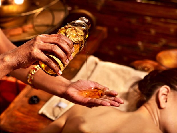 Женщина из Индии наливает на руку масло для проведения лечебного массажа