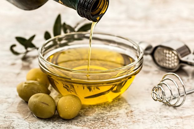 На столе мисочка с маслом оливы и рядом лежит четыре оливки