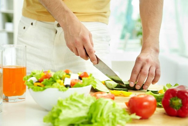 За кухонным столом человек нарезает полезные овощи для салата