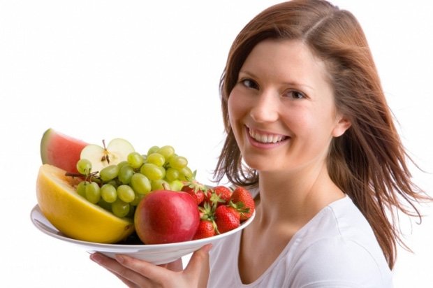 Улыбающаяся девушка держит в руках тарелку с фруктами