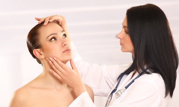 Женщина врач с темными волосами осматривает лицо пациентки
