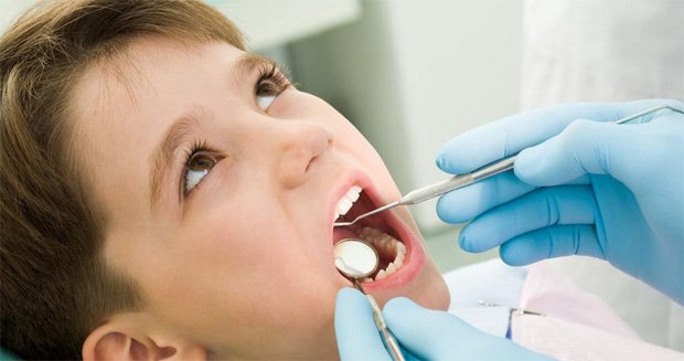 Врач стоматолог осматривает полость рта ребенка