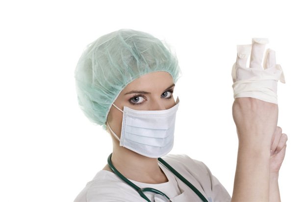 Девушка в защитной маске и шапочке надевает медицинскую перчатку