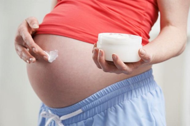 Беременная женщина наносит крем на свой живот