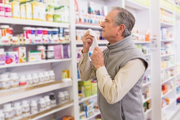Мужчина стоит в аптеке и разглядывает полки с препаратами
