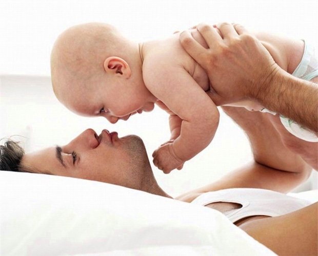 Молодой папа играет со своим ребенком на кровати