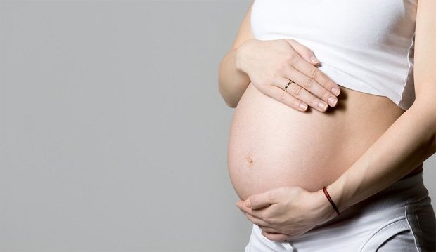 Беременная девушка держит себя двумя руками за живот